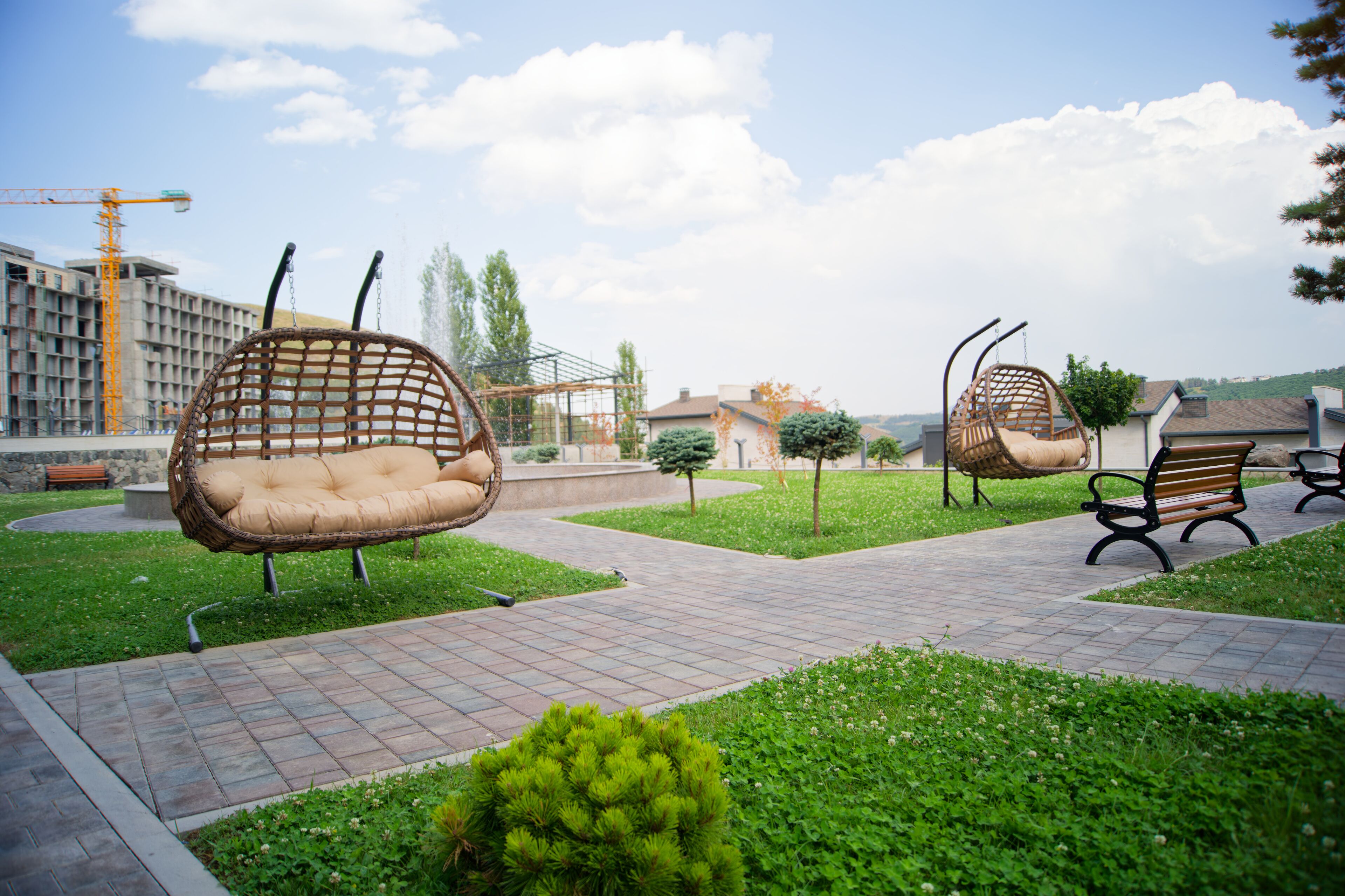 Un parque con sillas de mimbre, un sendero pavimentado y abundante vegetación.
