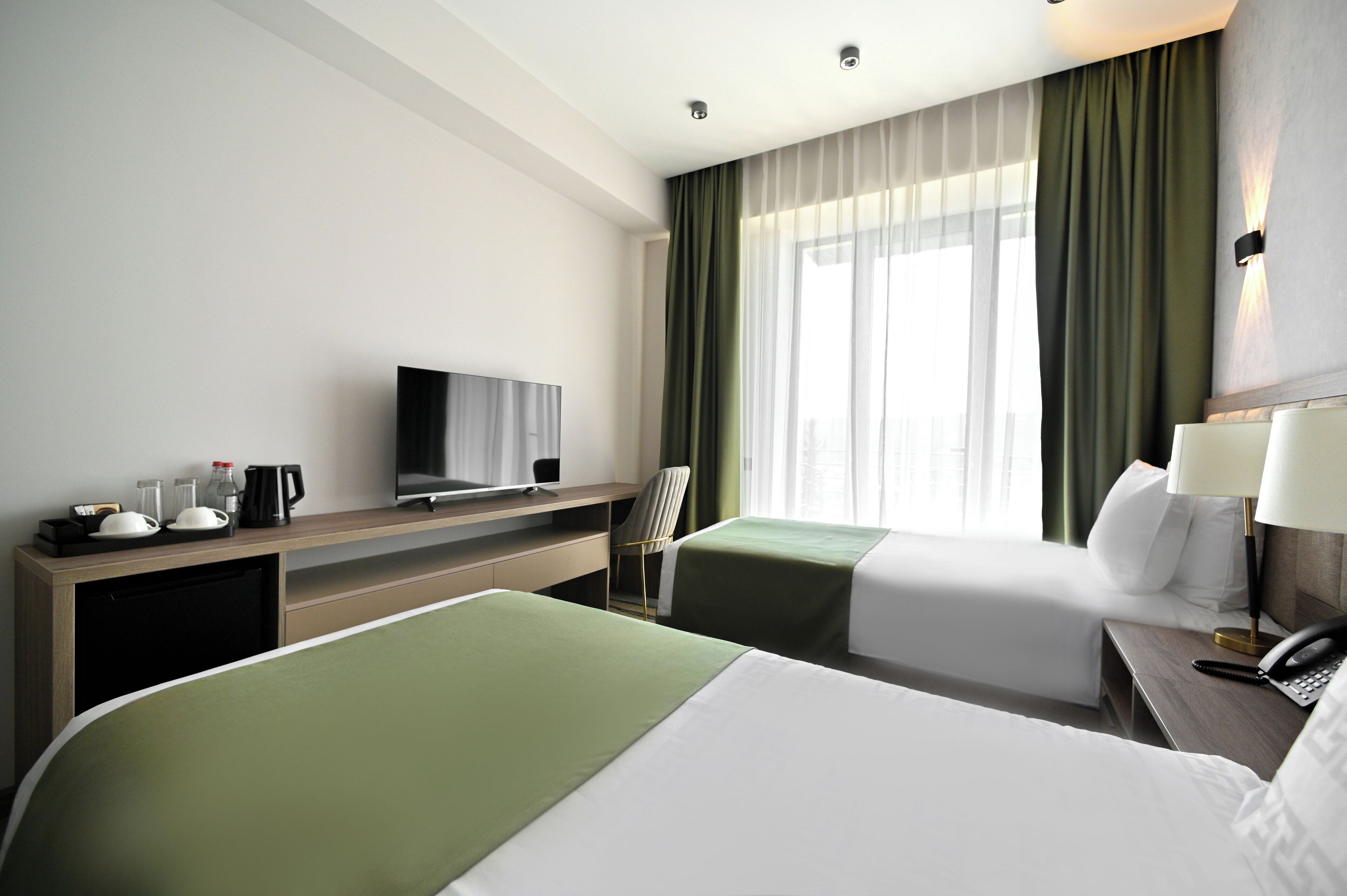 Habitación de hotel con dos camas, un escritorio con televisor, una silla y una mesita de noche con lámpara y teléfono.