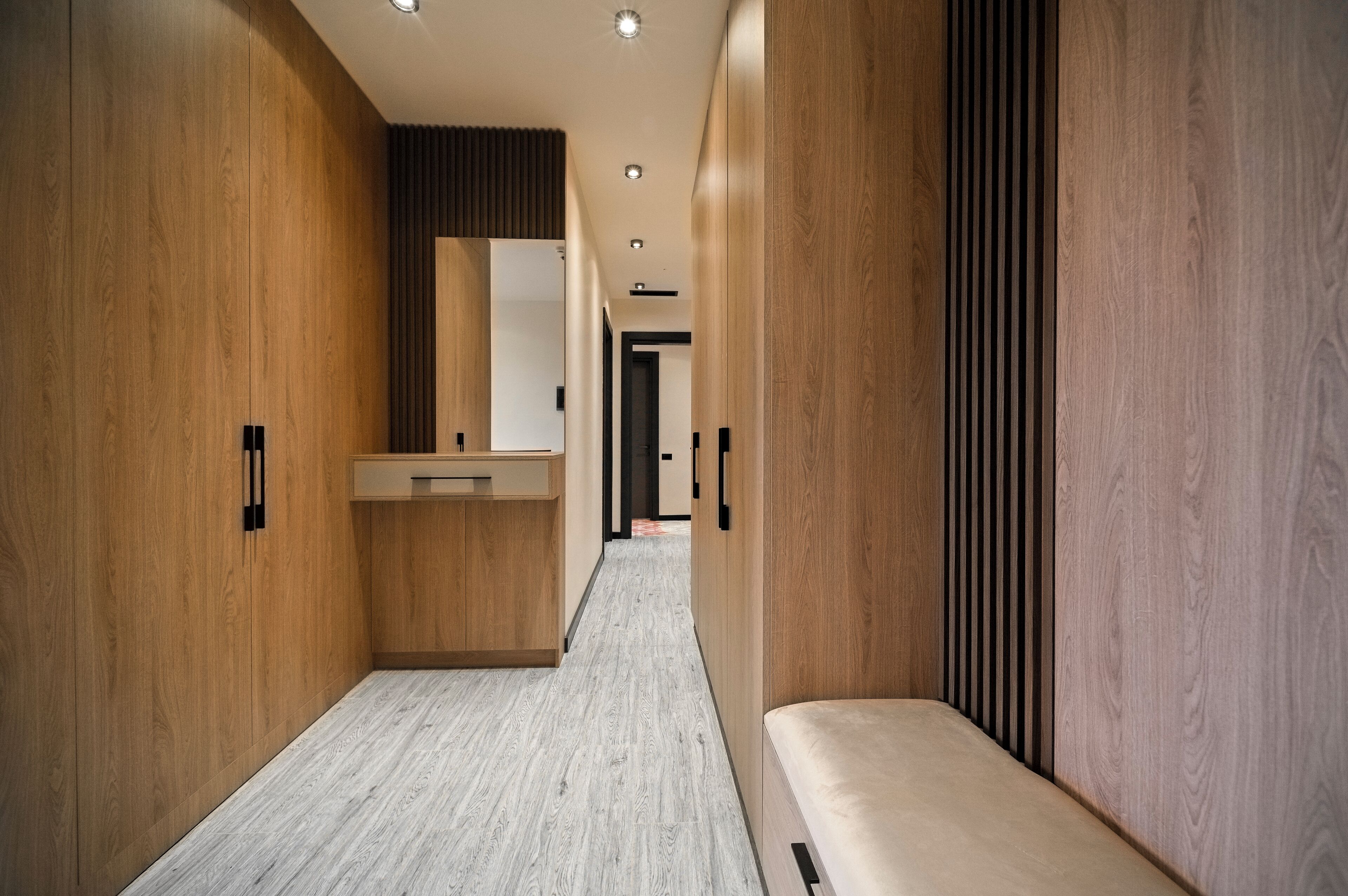 A modern hallway with wooden walls, a bench, and a central counter with a mirror.