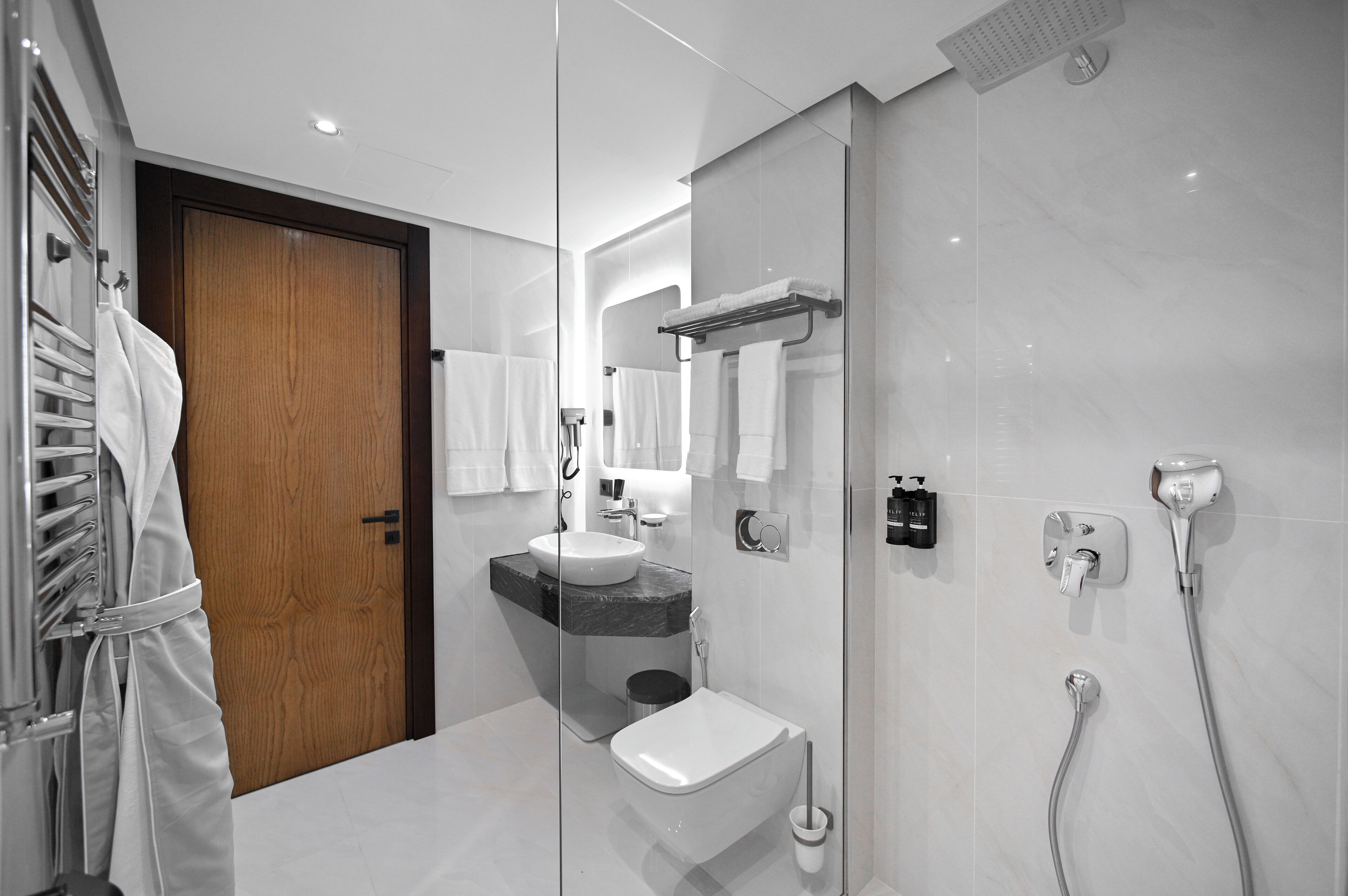 A modern bathroom with a wooden door, a sink, a toilet, and a shower area.