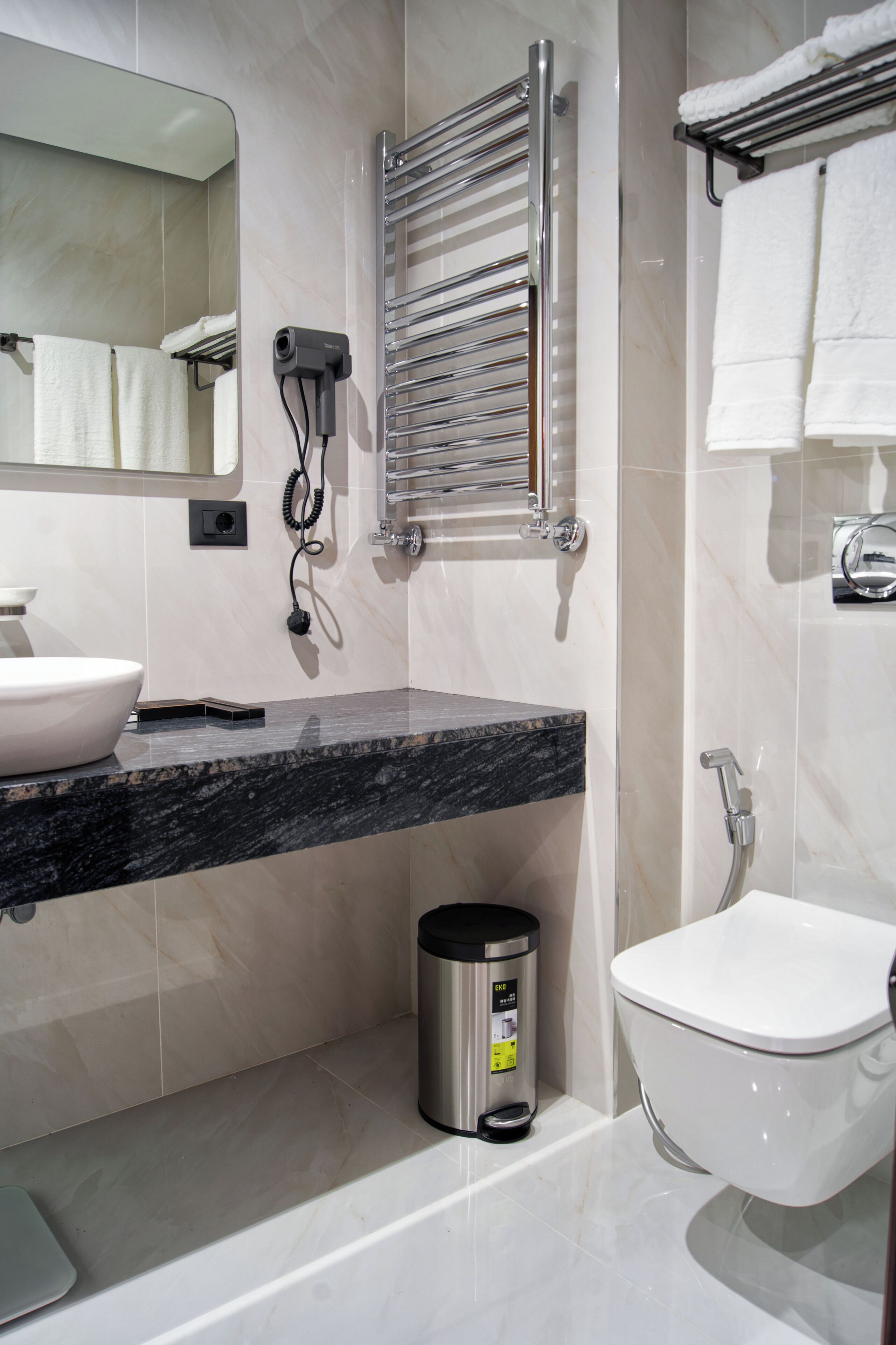 A modern bathroom with a marble countertop, a built-in sink, a toilet, a towel rack, and a hairdryer.