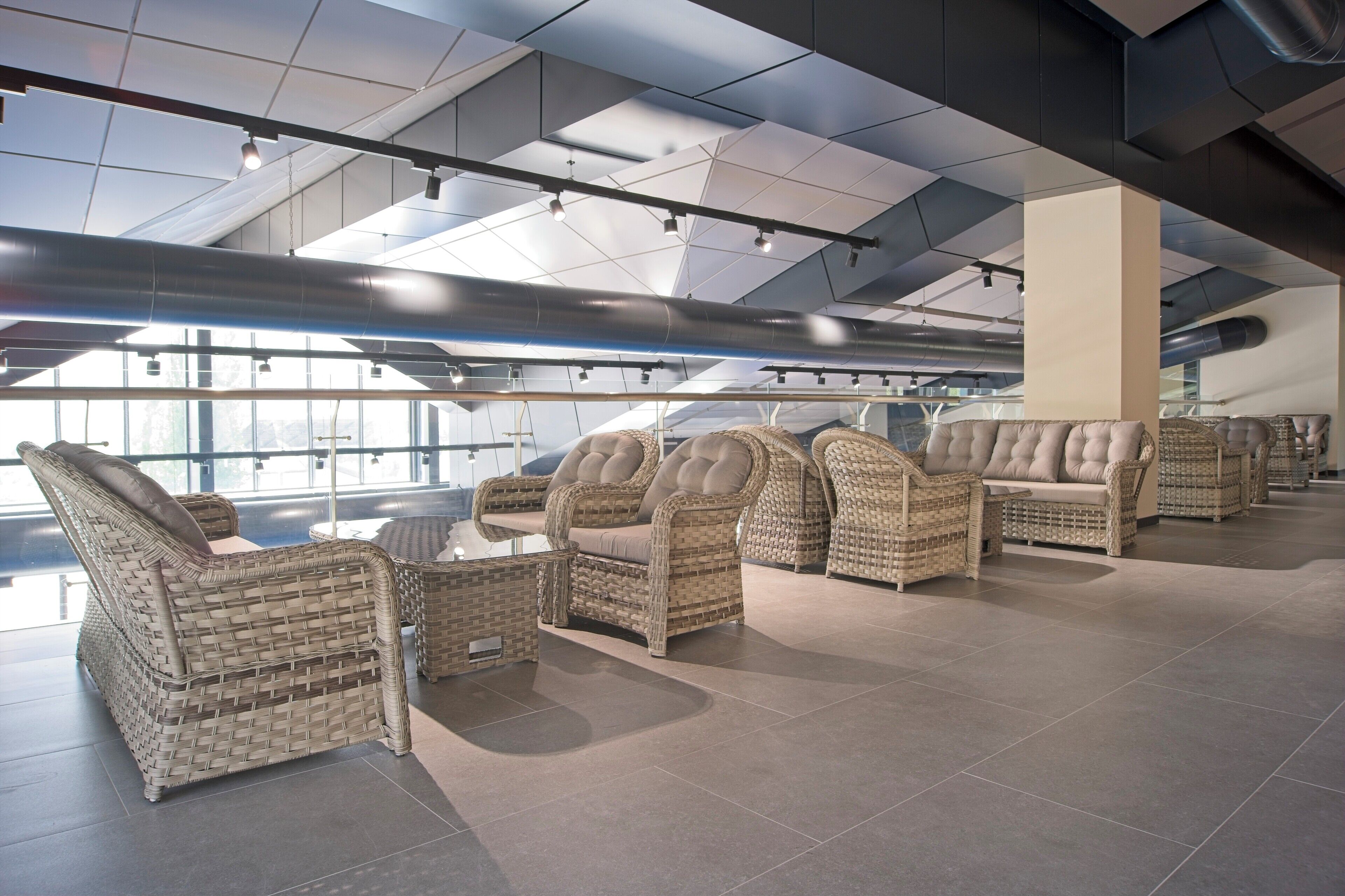 A modern lounge area with wicker furniture and a high ceiling with skylights.