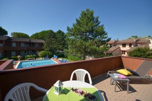 A rooftop pool area with lounge chairs, a table with a green tablecloth, and a view of the surrounding buildings and trees. - Relaxing retreat with pool (Bibione)