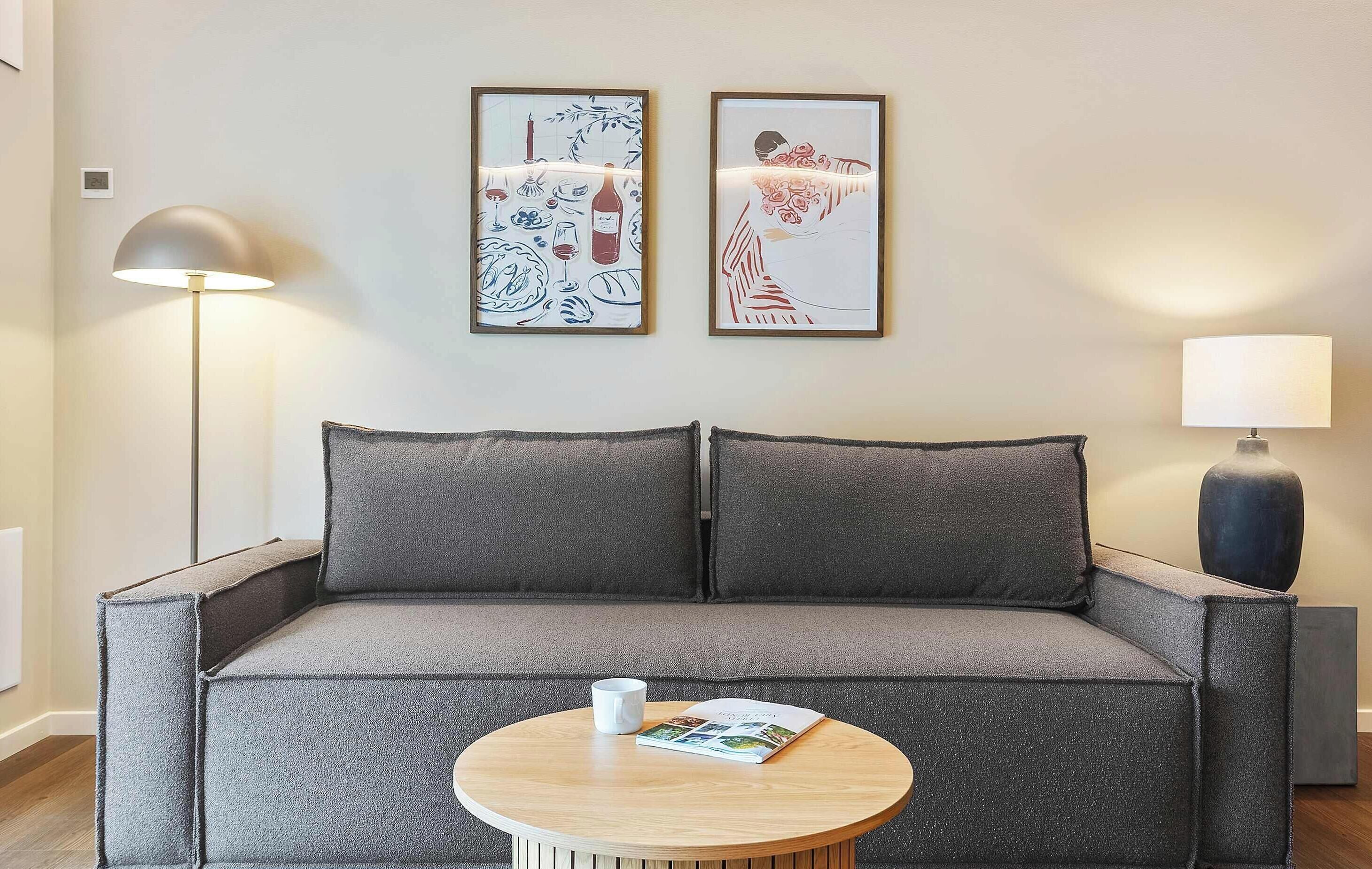Ein modernes Wohnzimmer mit einem grauen Sofa, einem runden Holztisch und zwei gerahmten Kunstwerken an der Wand.
