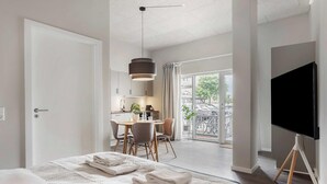 A hotel room with a bed, a TV, a dining area with chairs, a kitchen, and a balcony with a view. - Chic Ground-Floor Studio in Midtown (Aarhus)
