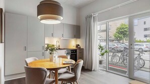A modern kitchen with grey cabinets, a wooden dining table, and a large window with a view of parked cars and bicycles. - Chic Ground-Floor Studio in Midtown (Aarhus)