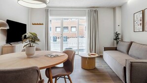 A modern living room with a sofa, a dining table with chairs, a TV, and a potted plant. - City Central Apartment w Modern Nordic Interiors (Aarhus)