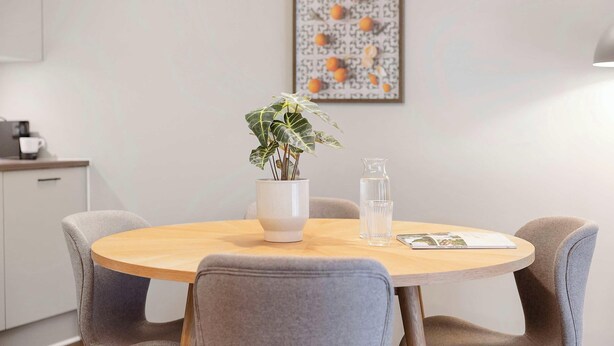 A round dining table with a white vase and a clear glass pitcher, surrounded by grey upholstered chairs. - City Central Apartment w Modern Nordic Interiors (Aarhus)