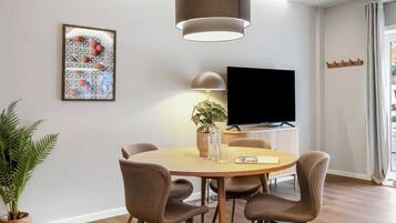 Een moderne eethoek met een ronde tafel, vier stoelen, een potplant, een flatscreen-televisie en een hanglamp.