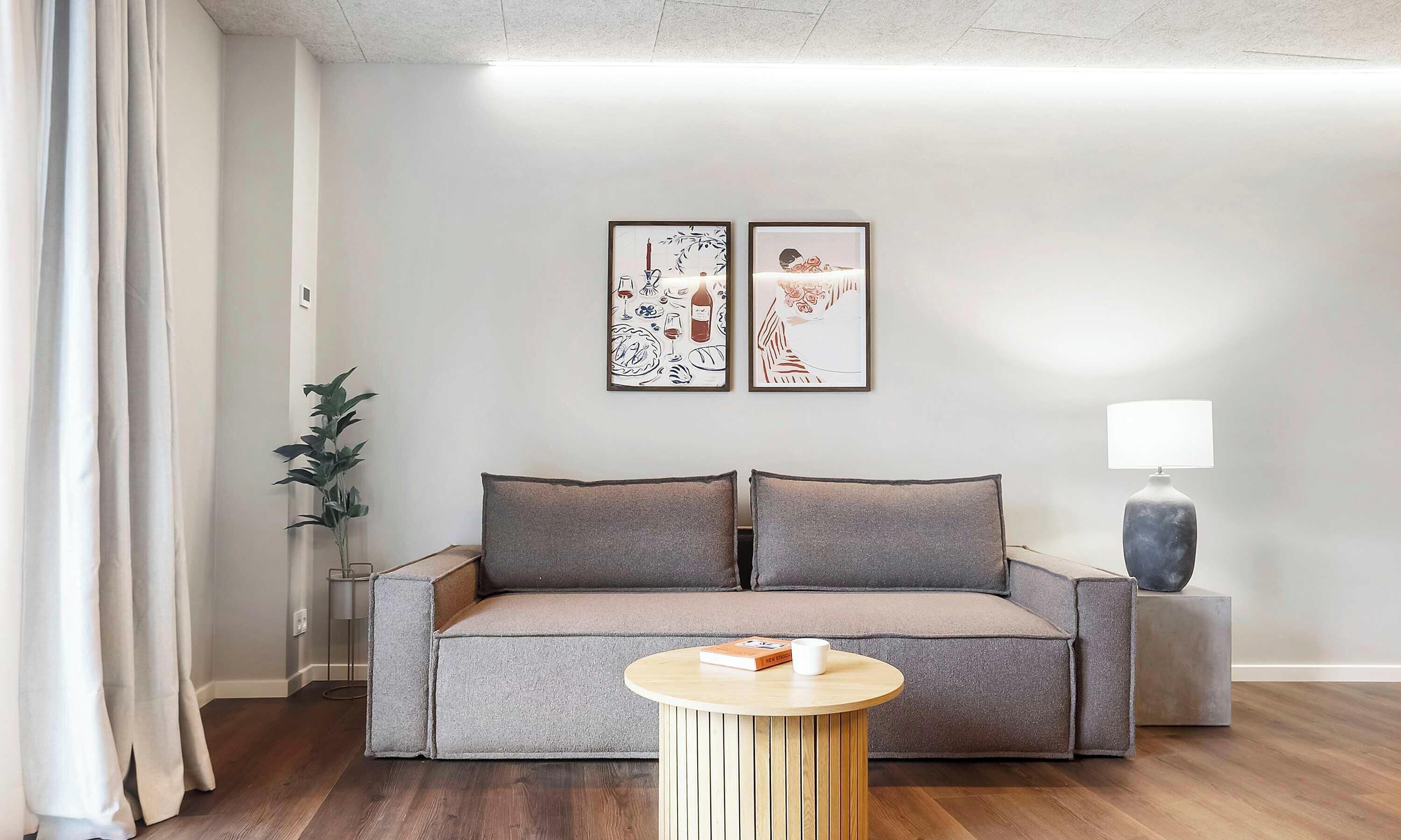 Een moderne woonkamer met een bank, een klein rond tafeltje, een lamp en twee ingelijste kunstwerken aan de muur.