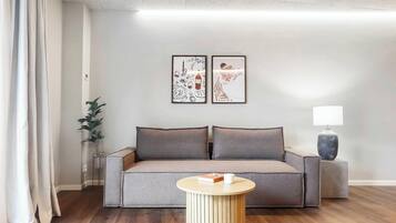 Een moderne woonkamer met een bank, een klein rond tafeltje, een lamp en twee ingelijste kunstwerken aan de muur.