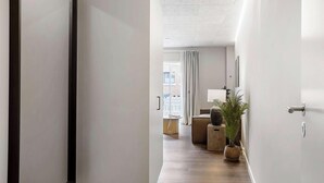 A hallway with a wooden floor, a potted plant, a lamp, and a view of a room with a window and curtains. - City Central Apartment w Modern Nordic Interiors (Aarhus)