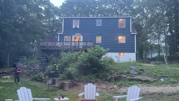 Et hus med en terrasse, et bålsted med stole og en stenvæg.
