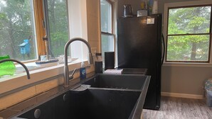Et køkken med en sort vask, et vindue og et køleskab.
