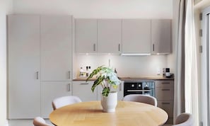 Eine moderne Küche mit einem runden Esstisch, einem Blumentopf und eingebauten Geräten.