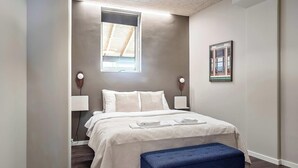 A bedroom with a bed, bedside lamps, a window, a framed picture, and a blue bench. - Ground-Floor Living with Stylish Nordic Interiors (Aarhus)