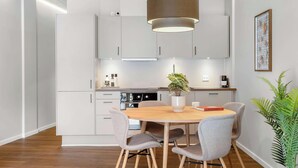 A modern kitchen with white cabinets, a central island with seating, a hanging light fixture, and a potted plant. - Ground-Floor Living with Stylish Nordic Interiors (Aarhus)