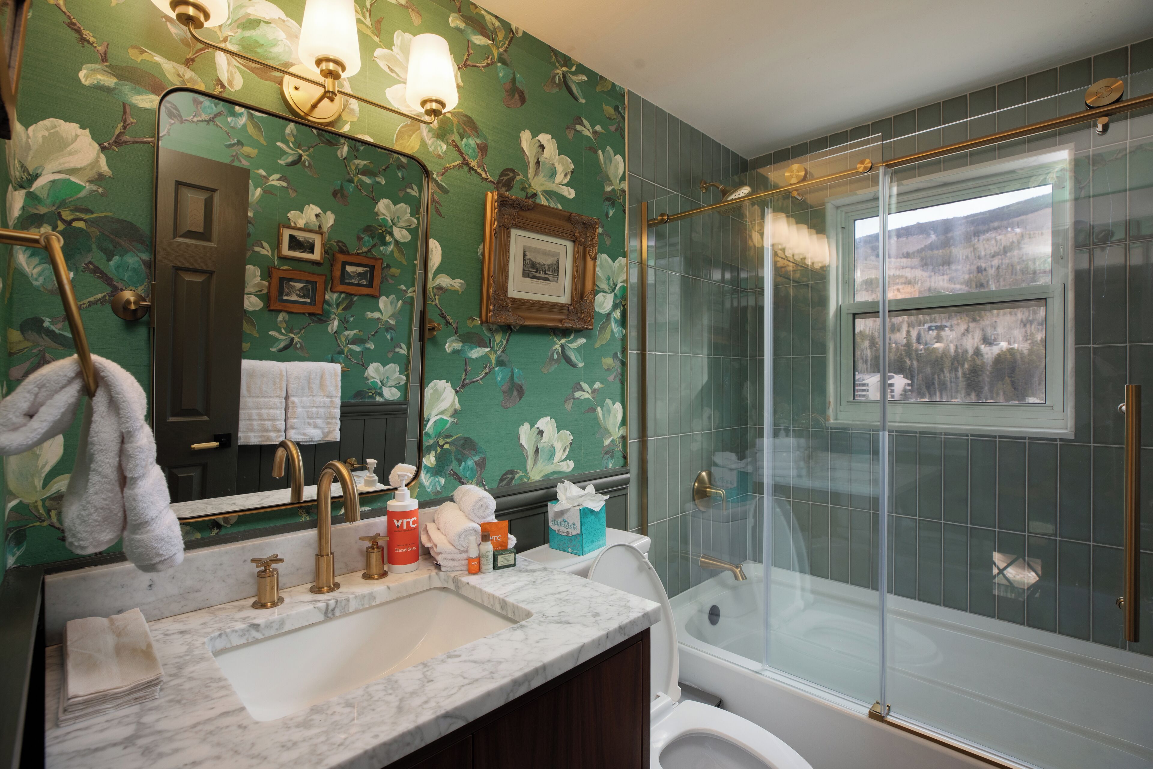 Une salle de bain avec un lavabo en marbre, une cabine de douche en verre et un papier peint à motifs floraux.