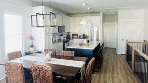 Una cocina moderna con armarios blancos, una isla central y un comedor con sillas de mimbre.