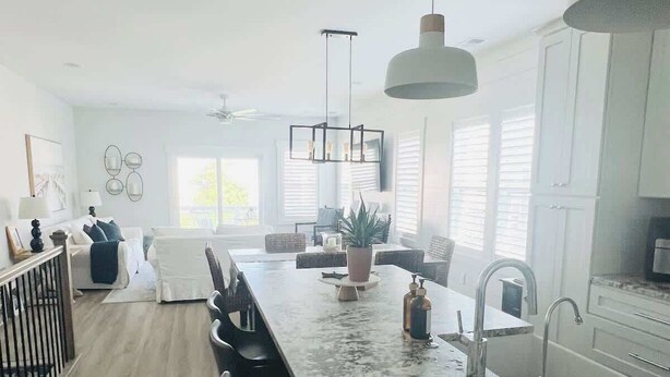 Una cocina moderna con una isla grande, luces colgantes y vistas al comedor.
