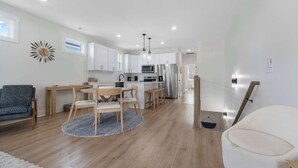 Una cocina moderna con armarios blancos, electrodomésticos de acero inoxidable y un comedor con sillas de madera y una mesa redonda.