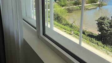A window with a view of a river, greenery, and buildings in the distance.