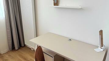 A minimalist room with a white desk, a brown chair, a radiator, and a shelf with a small item on it.