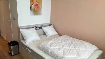 A bedroom with a bed, a trash bin, and a wall-mounted picture.