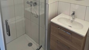 Un bagno moderno con doccia vetrata, lavandino bianco e mobile contenitore in legno.