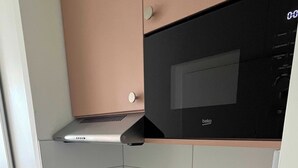 Una cucina compatta con un forno a microonde nero, un lavello in acciaio inossidabile e una moka su un tappetino nero.