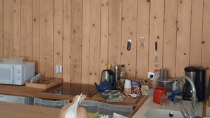 A kitchen with wooden cabinets, a microwave, a kettle, and various kitchen utensils.