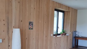 A room with wooden panel walls, a window with potted plants, and a white lamp on a wooden table.