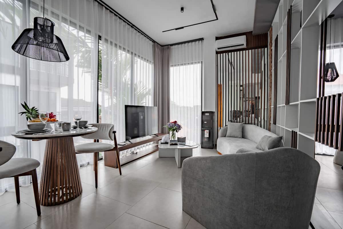 A modern living room with a sofa, a dining table with chairs, a TV, and a decorative plant.