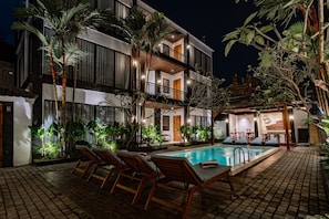 Un hotel moderno con piscina, sillas de descanso y plantas tropicales.