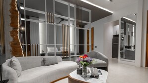 Een moderne woonkamer met een grijze bank, een houten bijzettafeltje en een vaas met bloemen.