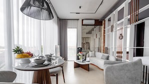 Een moderne woonkamer met een ronde eettafel, grijze banken en een groot raam met lichte gordijnen.