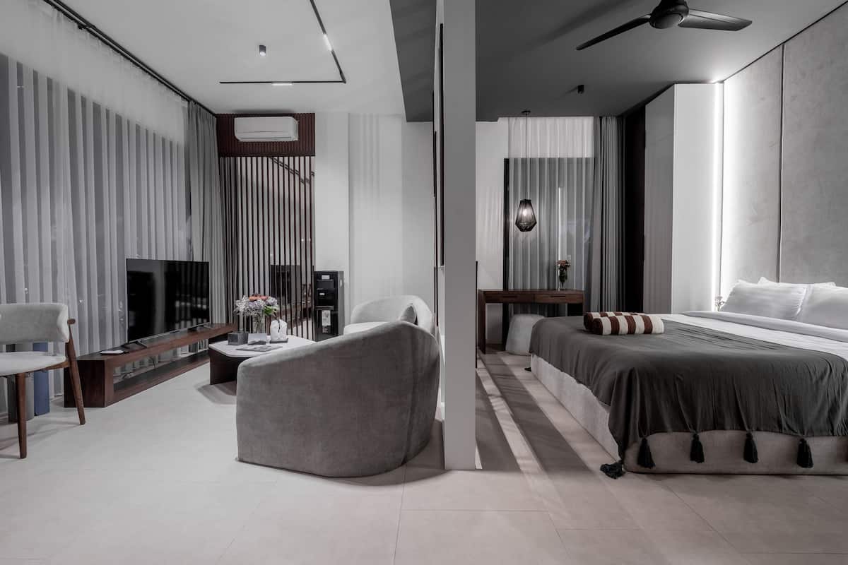 A modern hotel room with a large bed, a seating area with a sofa and armchair, a TV, and a small table with a vase of flowers.