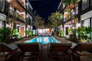 Un espace piscine doté de chaises longues, entouré d’immeubles avec des balcons et des portes en bois.