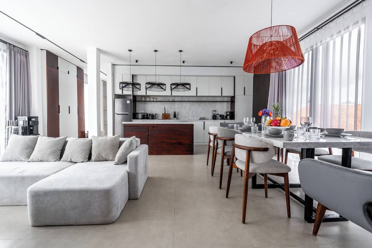 A modern kitchen with a central island, a dining area with a long table and chairs, and a large window with curtains.