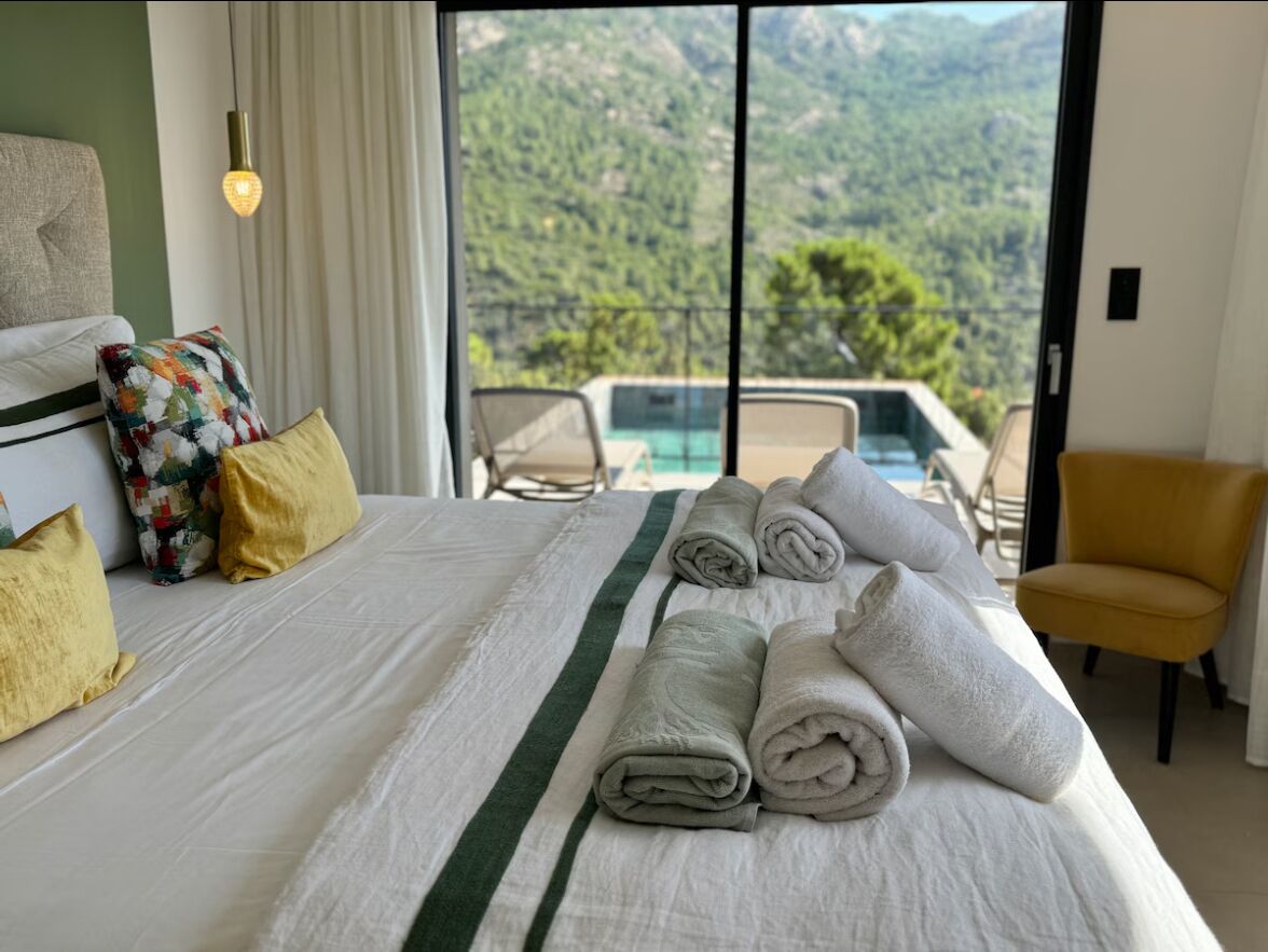 Une chambre d’hôtel avec un lit, un fauteuil jaune et une vue sur un paysage montagneux.