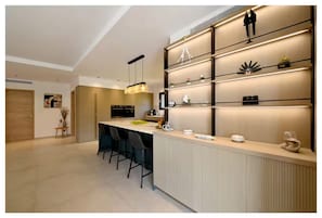 A modern kitchen with a central island, bar stools, pendant lighting, and built-in shelves with decorative items. - Exclusive new villa with breathtaking views (Zonza)