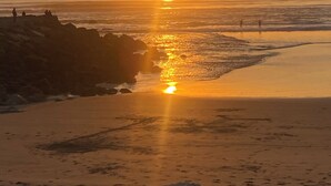 A beach scene with the sun setting over the ocean, casting a golden glow on the water and sand.