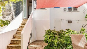 A narrow staircase leading to a white door, surrounded by greenery and a red shade sail.