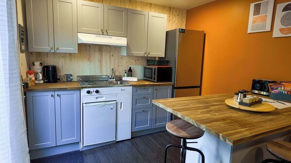 A compact kitchen with white cabinets, a stove, microwave, and a refrigerator. - La Cabane Sereine | SPA Privé (Rouyn-Noranda)