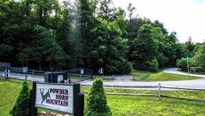 A sign for Powder Horn Mountain with a deer silhouette, surrounded by greenery and a fenced area.