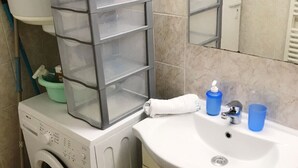 Ein Waschbereich mit Waschmaschine, Wäscheständer und Waschbecken mit Spiegel darüber.