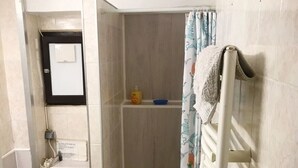 Ein Badezimmer mit Toilette, einer Duschkabine, einem Handtuchhalter und einem kleinen Ablagefach für Toilettenartikel.