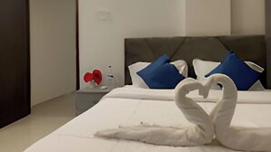 A modern hotel room with a neatly made bed, a headboard, and a bedside table with a red object on it. - Ashwa Glory Retreat (Igatpuri)