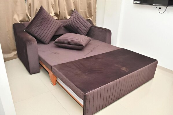 A modern sofa bed with a matching ottoman, a flat-screen TV mounted on the wall, and a curtain in the background.