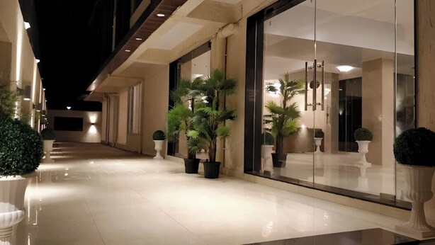 A well-lit corridor with potted plants, a glass door entrance, and a clean, reflective floor. - Ashwa Glory Retreat (Igatpuri)